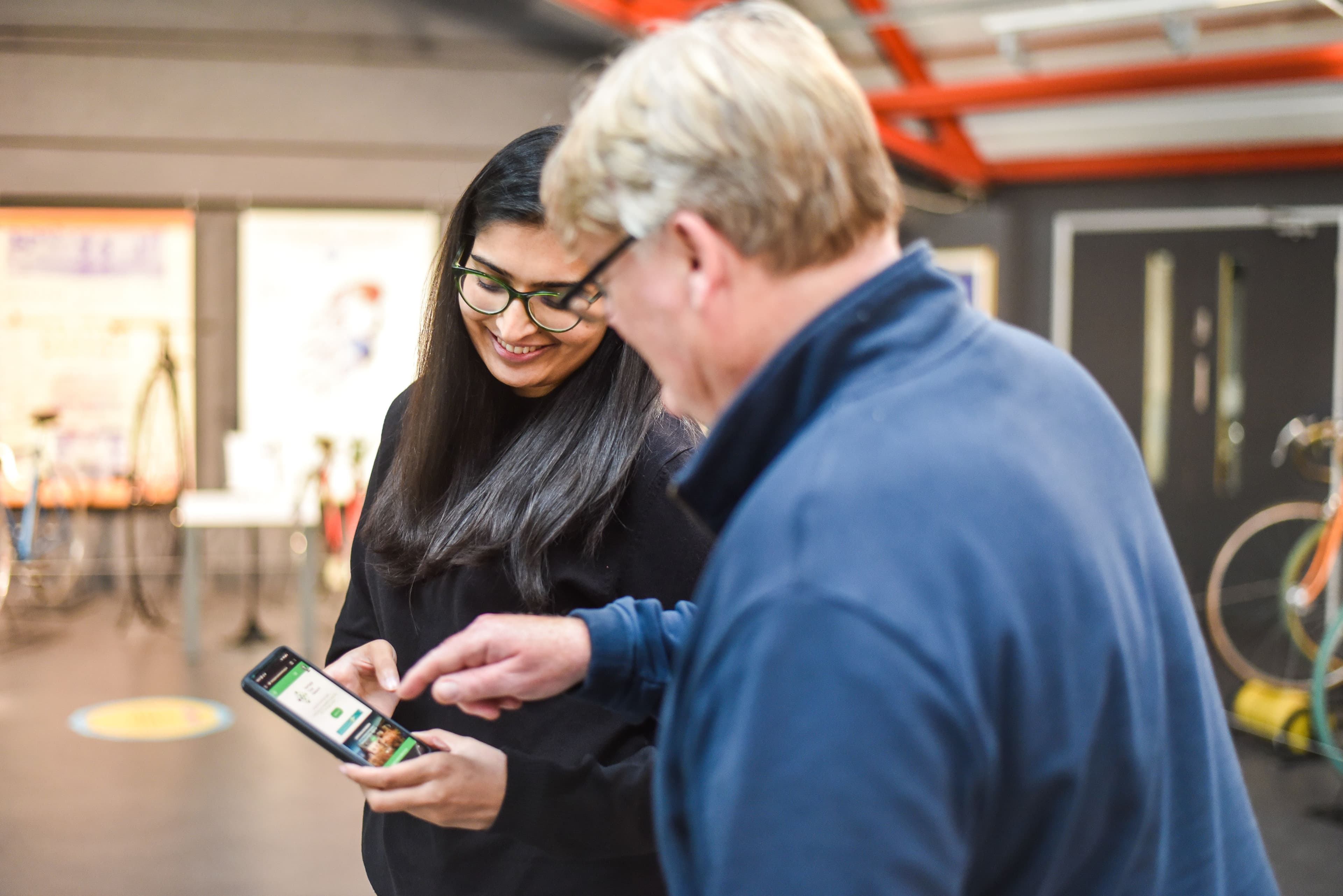 A young person is showing a mobile phone to an older person who is pointing at the screen.