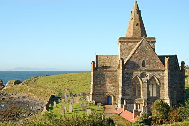 Exterior of St Monans Kirk. The church sits in front of a field and text to a beach.