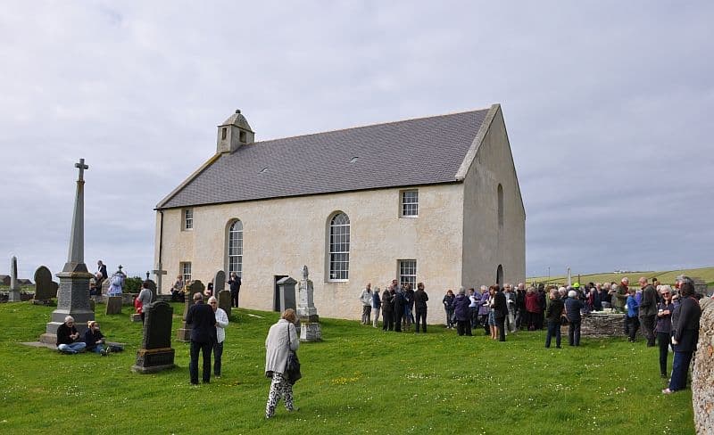 Exterior of St Magnus with people sat and stood around in the graveyard.